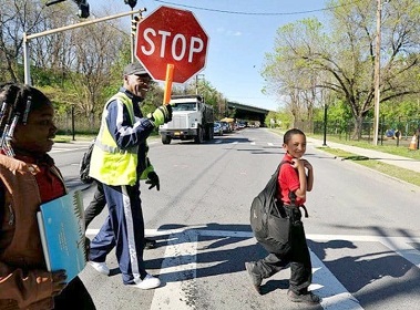 A man holding up a lollipop sign to help children cross a road